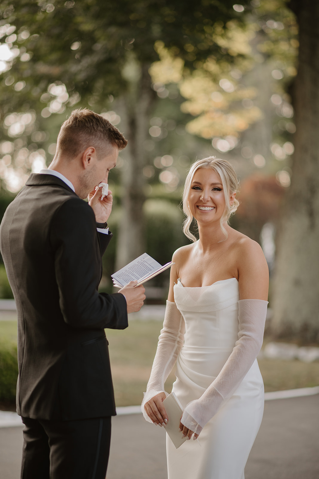 Bride smiles brightly while the groom wipes away a tear during their emotional private vow exchange.